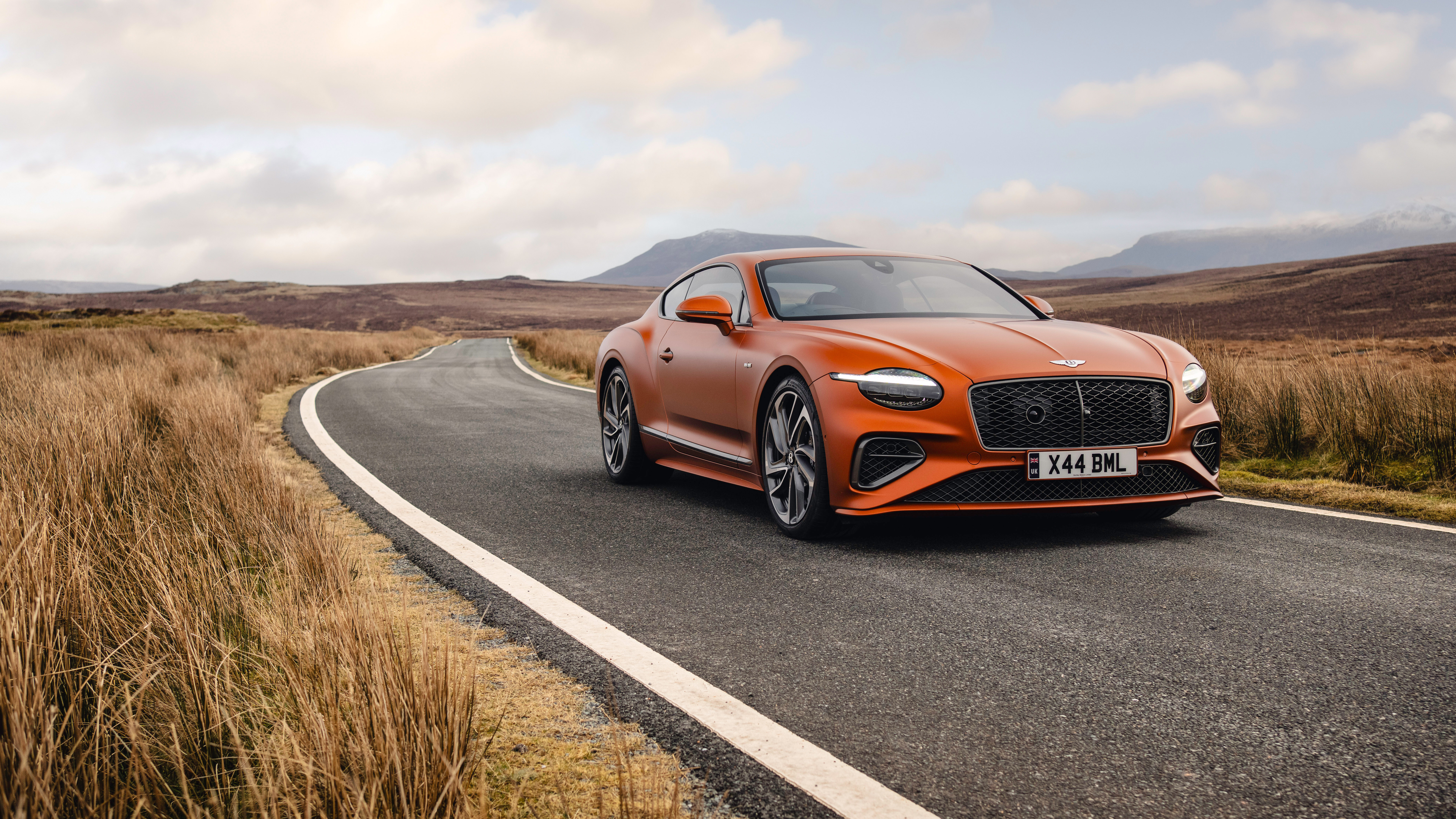 Efektowny, pomarańczowy Bentley Continental GT Speed, prezentujący swoje luksusowe wnętrze i potężną sylwetkę.